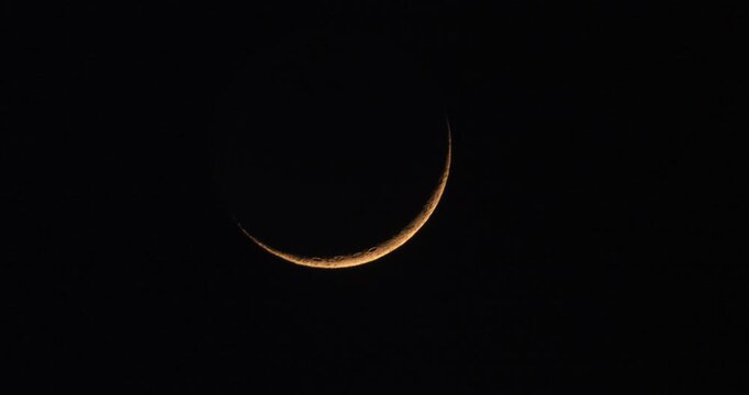 Timelapse of young crescent moon movement during moonset with passing clouds