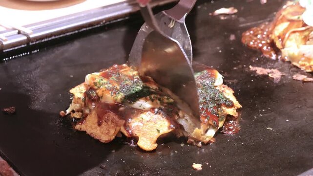 Okonomiyaki on a sizzling hot pan. Okonomiyaki is a savory Japanese pancake made from a flour batter mixed with cabbage, egg, and other fillings like meat or seafood
