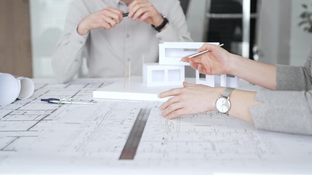 Architects and designer planning a modern house building project, collaborating on construction blueprints and architectural model in a professional office, close up