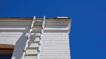 Fototapeta premium Metal ladder leaning against a white wall under blue sky 
