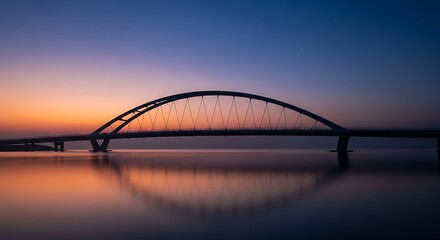 Obraz premium Arch bridge over calm waters at sunset.
