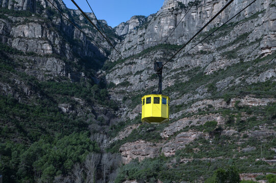 Iconic yellow Aeri de Montserrat cable car ascending the rugged jagged peaks of Montserrat mountain in Catalonia, Spain, under a clear blue sky
