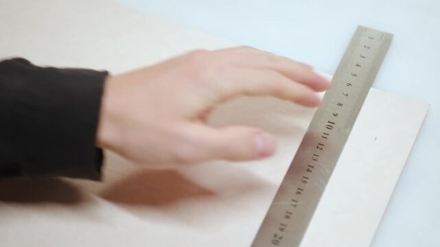 Handheld close up of craftsman marking straight guideline on material using metal ruler and pen. Focus on precise measurement and careful preparation stage in artisan workshop.