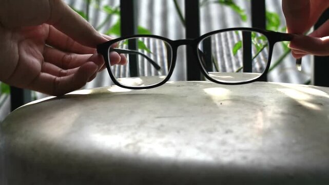 Black frame eyeglasses opened by hands facing camera then placed on rusty white metal surface