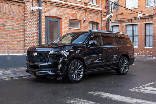 New Cadillac Escalade parked in the city near a red brick building. Full-size luxury SUV with bold design and premium presence, captured in modern urban automotive photography style