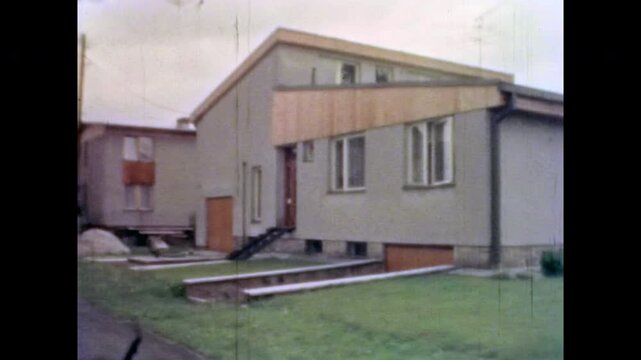 Modern private house exterior in spring. Green, well-kept lawn surrounds house. No people. Contemporary residential architecture with clean landscape. Old film. Archival retro 1970s. Vintage archive