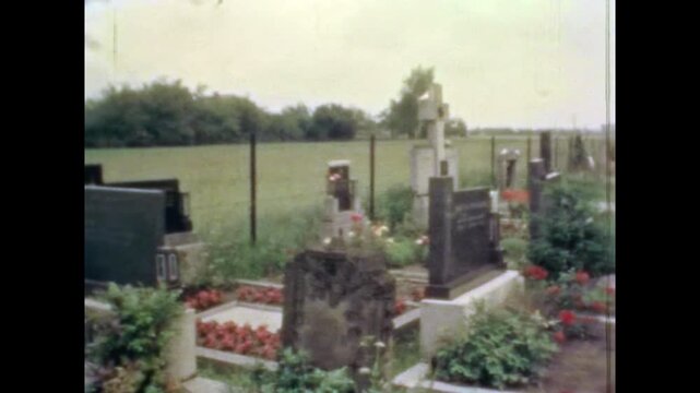 Wide view, European city cemetery in spring. Rows of headstones and tombstones surrounded by green lawn landscape. Peaceful burial ground in urban. Old film. Archival retro 1970s. Vintage archive