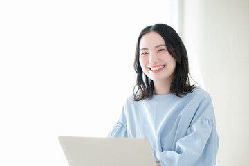 明るい部屋でパソコンで仕事や検索、調べるお洒落な女性　資格や勉強などのスキルアップ、キャリアアップの前向きなポジティブイメージカメラ目線