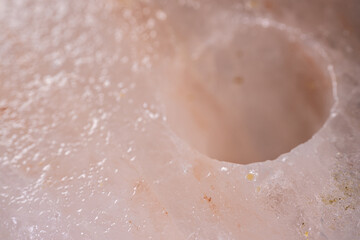 Fototapeta premium Close-up view of a translucent pink Himalayan salt block with a circular hole, showcasing the unique crystalline structure and texture of the mineral