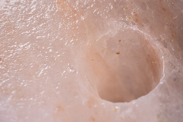 Fototapeta premium Close-up view of a pink Himalayan salt block with a circular indentation, showcasing the unique texture and mineral inclusions of the natural salt formation