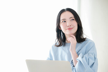 明るい部屋でパソコンで仕事や検索、調べるお洒落な女性　資格や勉強などのスキルアップ、キャリアアップの前向きなポジティブイメージ顎に手を当てる考える悩む