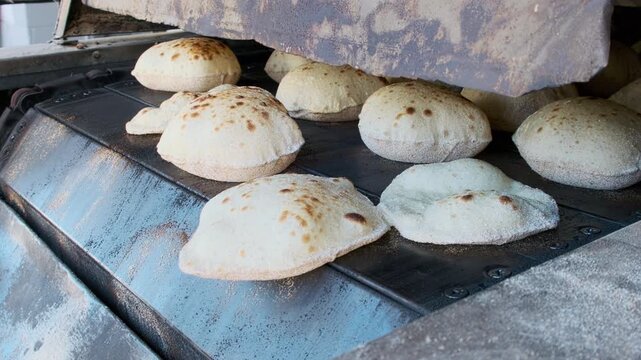Close-up footage of traditional egyptian flatbread aish baladi baking in conveyor oven. Baking pita bread on traditional egyptian street baker shop