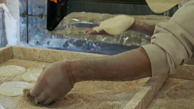 Hands of baker putting traditional egyptian flatbread aish baladi to conveyor oven. Baking pita bread on traditional egyptian street baker shop