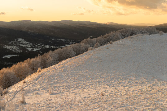 Scenic winter landscape of frosted mountain meadows and hills glowing in the golden light of a sunset or sunrise. Trail to Smerek, Bieszczady National Park, Poland.