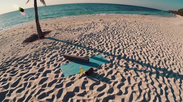 A wide-angle beach scene shows rippled white sand, a lone palm casting a long shadow, and a surfboard beside a teal towel near the shore, with turquoise waves rolling under a clear sky.