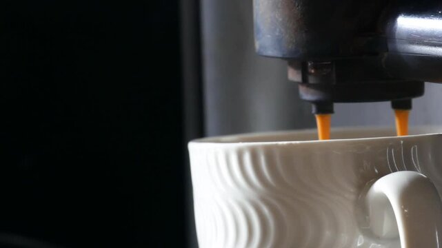 Coffee brewing into a white cup from an espresso machine, showing the process of making a beverage.