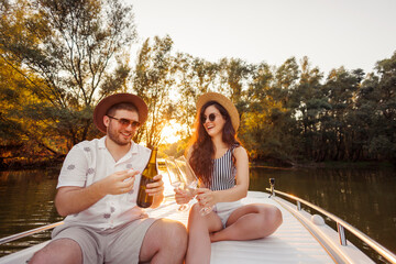 Couple celebrating anniversary opening a bottle of champagne while sailing on a boat in sunset © Impact Photography