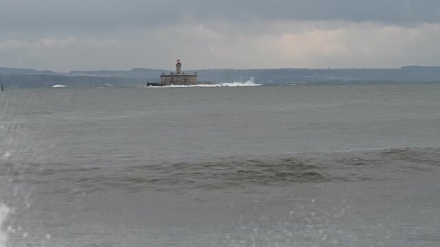 Large ocean wave breaking beside Bugio lighthouse