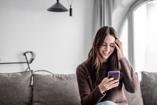 Portrait of smiling woman in video call to friends or relatives, using phone webcam, sitting on couch at home, happy young female blogger recording vlog, chatting online