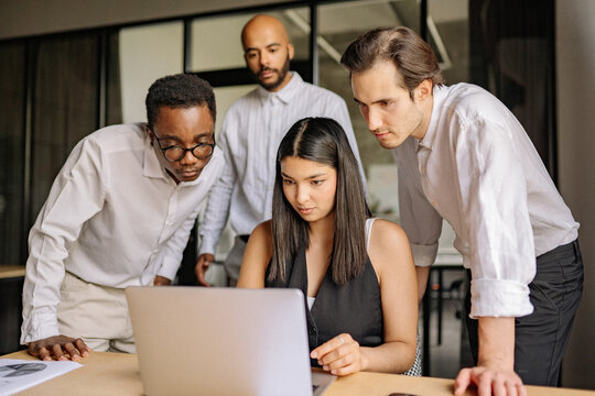 Group of diverse professionals collaborate on a project while analyzing data on a laptop in a modern office setting during the daytime