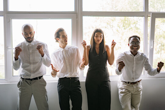 Diverse team enjoying a joyful moment while dancing and laughing near large windows in a bright, airy room during a sunny daytime gathering