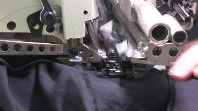 Hand of the seamstress is using white industrial sewing machine sew zipper (slide fastener). Sewing workshop. Sewing zipper on sewing machine.
