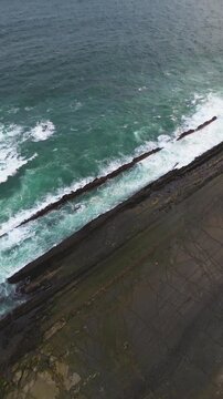 Clean aerial perspective facing the open ocean horizon at Sawarna Beach, Indonesia. Gentle waves meet the coastline under soft sky tones, recorded in smooth Vertical drone footage.