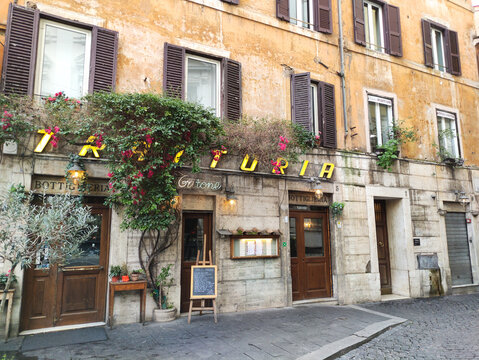 Rome, Italy - February 20, 2026: Italian trattoria with rustic wooden doors and vibrant greenery on a cobblestone street in Rome, Italy