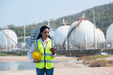 portrait of a female worker. female construction worker. person in helmet using radio communication. person in helmet with oil tanks in the desert on background.	