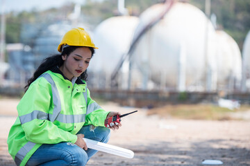portrait of a female worker. female construction worker. person in helmet using radio comunication. person in helmet with oil tanks in the desert onbackground.	
