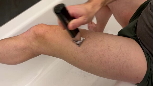 Man trimming his hairy legs with an electric trimmer in a bathtub, modern male grooming routine at home, intimate bathroom lifestyle scene.