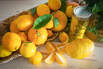 Various lemon fruits in a basket and fresh rosemary on white vintage wood. Freshly preserved lemon wedges in a glass jar.