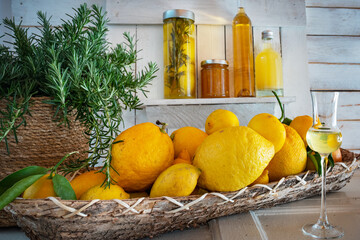 Various lemons in a basket with fresh rosemary on white vintage wood. Preserved lemon wedges in a jar, limoncello lik&ouml;r, vinegar, and marmalade. 