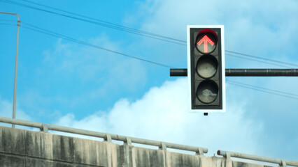 Traffic light sign with a red light indicating that proceeding is prohibited. Perched on black steel pillars with the concrete bridge railing as a backdrop under a blue sky.