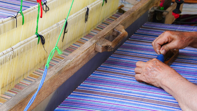A craftsman tying plastic strings on silk threads to create traditional Thai Mudmee (ikat) patterns before dyeing. Handmade silk weaving process showing Thai culture, craftsmanship, and textile art.