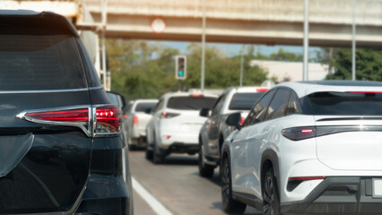 Fototapeta premium Rear side view of back car with turn on brake light on the road. Traffic conditions on the road with many cars parked in a queue. Background blurred of concrete bridge and trffic light green color.
