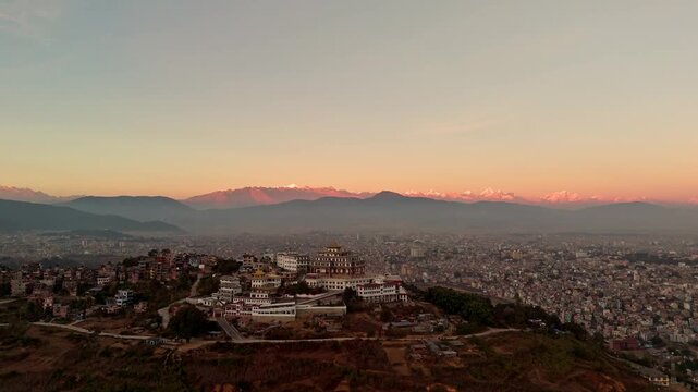 Aerial Drone Shot of Buddhist Monastery Above City with Mountain Range at Sunset