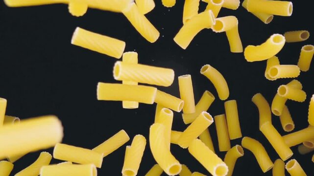 macaroni pasta peaces falling down from above in black background 