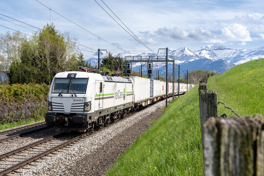 Spiez, Switzerland - April 27, 2023: Railcare / Coop freight train near Spiez in spring, passing through the Bernese Oberland with snow-capped mountains and fresh alpine scenery.
