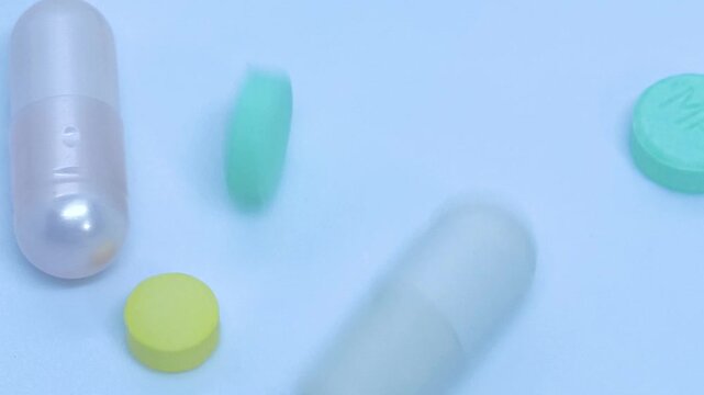 4k slow moition video footage. The round pills and capsules are falling one by one onto the white surface.