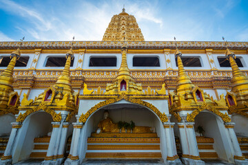 Golden Buddha statue at Phutthakhaya Chedi in Sangkhla Buri, Kanchanaburi, Thailand beneath a dramatic blue sky