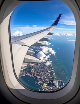 Aircraft wing and city view seen through the plane window, below sky with clouds over ocean