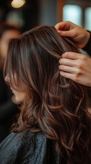 Fototapeta premium The stylist carefully styles the client's long hair in the beauty salon, emphasising professionalism and care, which is ideal as an atmospheric backdrop for advertising hairdressing services.