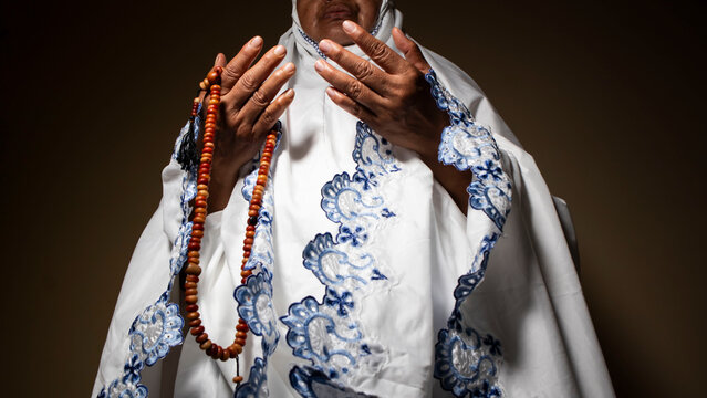 a women wearing mukena is praying with prayer beads during fasting and eid mubarak