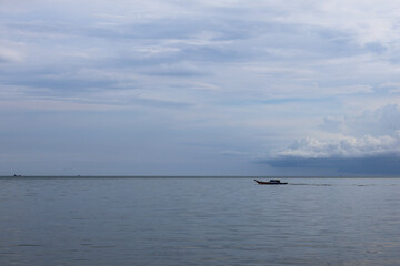 Obraz premium Traditional wooden motorboat sailing on the calm blue sea under a cloudy sky at daytime in tropical horizon.