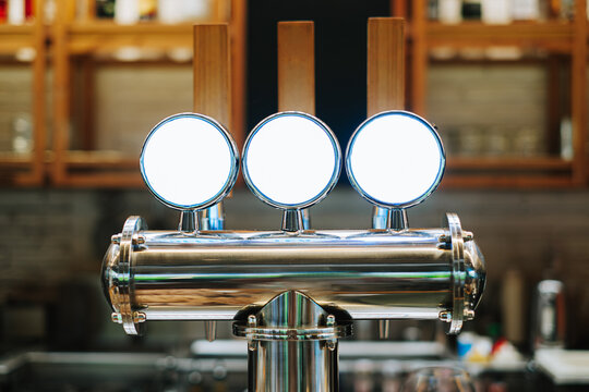 Three polished chrome draft beer or nitro cold brew taps with blank white labels in a bar