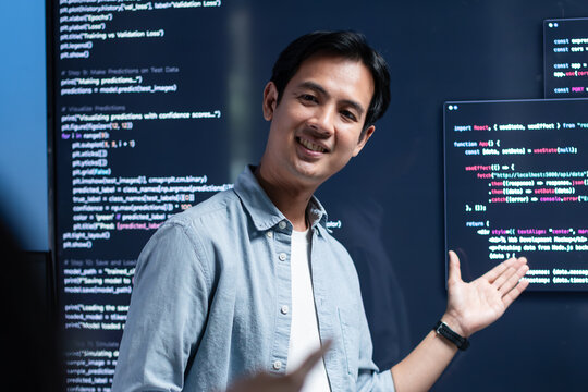 Asian male software engineer presenting source code on large screens in a modern tech office, explaining solutions in a team meeting. Concept for coding, code review, agile workflow.