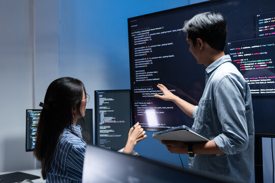 Female and Male Software Developer, Computer Programmer pointing to screen while software development meeting session, Two Developer brainstorming working on code task, AI Project in office at night.