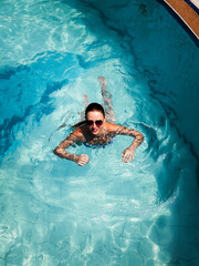 Healthy woman relaxing while floating in crystal clear pool water under warm sunlight. Active lifestyle and wellness concept with calm leisure, refreshing summer escape, peaceful mood and natural
