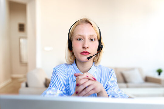 Customer support concept. Portrait of young blonde woman in headset with clasped hands looking at camera. Professional female operator working from home or providing online technical assistance.